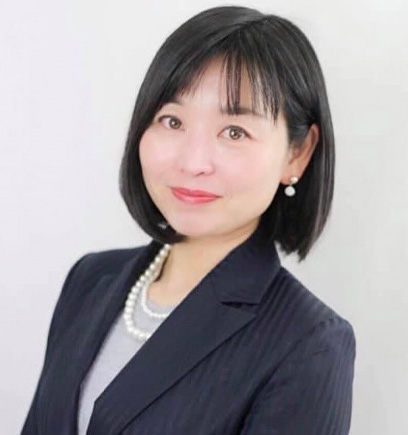 Head-and-shoulders portrait of an Asian woman in a navy blazer, white blouse, pearls, smiling at the camera.